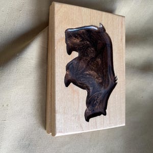 May include: A wooden block with a horse head silhouette filled with a dark, swirled resin. The wood has a light, natural finish, and the resin has a glossy, marbled appearance. The horse head is a prominent feature.