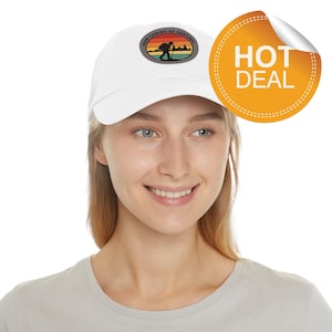 May include: A white baseball cap with a patch featuring a hiker silhouetted against a sunset, with the text "Buen Camino de Santiago." An orange "HOT DEAL" sticker is visible.