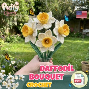 以下が含まれることがあります： 白い花びらと黄色の中心を持つかぎ針編みの水仙のブーケ。ガラスの花瓶に入っています。「Daffodil Bouquet Crochet」の文字がピンクと緑で書かれています。蝶と「Puffy Cherry」のロゴも表示されています。