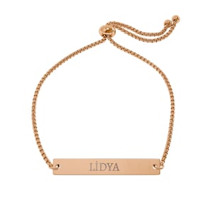 May include: Rose gold adjustable bracelet with a rectangular bar engraved with the name "LIDYA". The bracelet features a delicate chain and a sliding bead closure for a customizable fit. A stylish piece of jewelry.