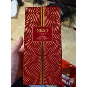 May include: A rectangular red box for a Nest Fragrances Holiday reed diffuser. The box features a gold geometric pattern and a central gold label with the text NEST FRAGRANCES NEW YORK HOLIDAY REED DIFFUSER DIFFUSEUR DE PARFUM 5.9 fl oz e 175 ml.