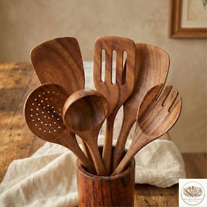 May include: A collection of wooden kitchen utensils, including a slotted spoon, spatula, and ladle, displayed in a wooden holder. The utensils are made of a warm-toned wood and are arranged against a neutral background.