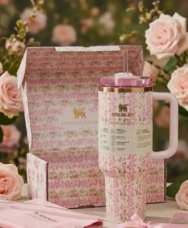 May include: A floral-patterned Stanley Loveshackfancy tumbler with a pink lid and handle, presented with a matching box and straw. The tumbler features the Stanley and Loveshackfancy logos. The design includes pink and white flowers.