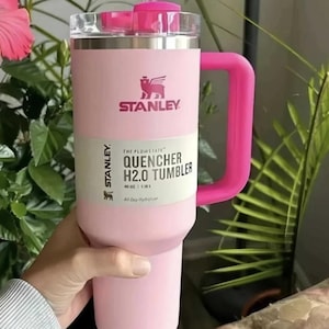 May include: A pink Stanley Quencher H2.0 Tumbler with a handle. The tumbler has a clear lid and a pink straw. The text on the tumbler reads "STANLEY" and "QUENCHER H2.0 TUMBLER". It holds 40 oz (1.18 L).