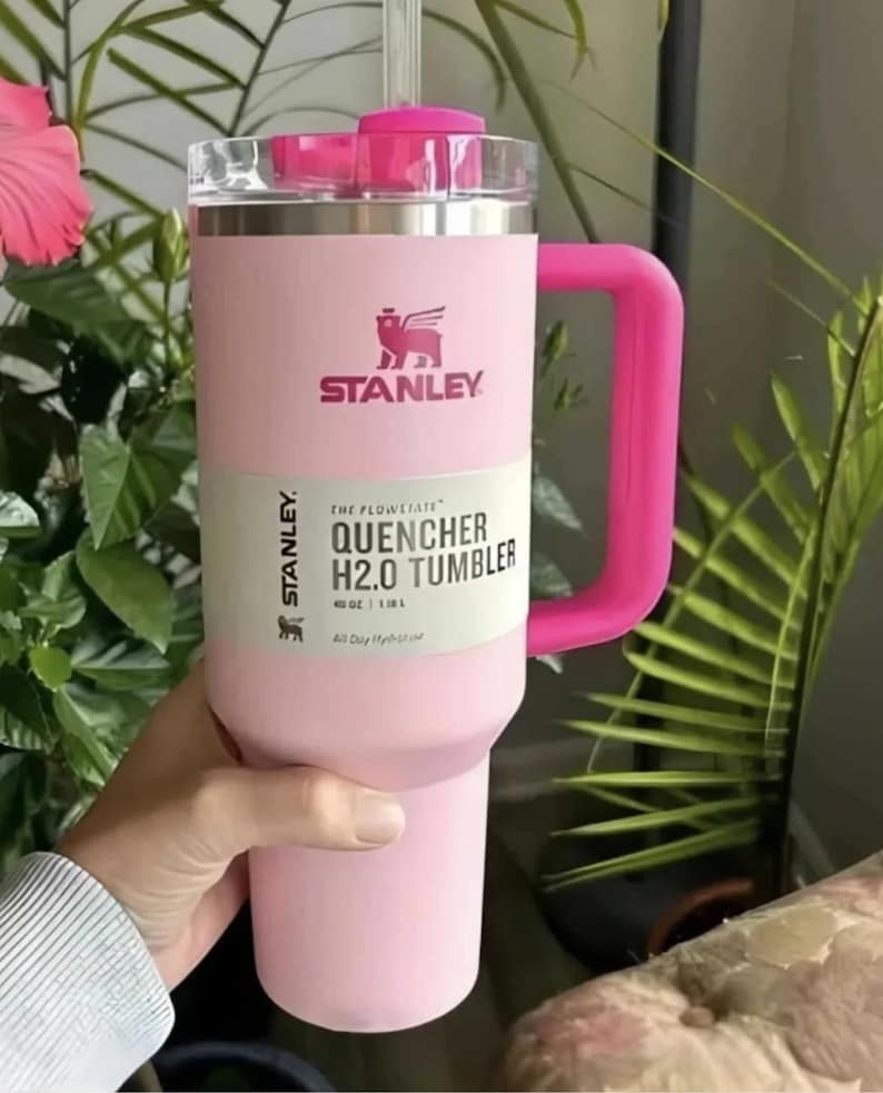 May include: A pink Stanley Quencher H2.0 Tumbler with a handle. The tumbler has a clear lid and a pink straw. The text on the tumbler reads "STANLEY" and "QUENCHER H2.0 TUMBLER". It holds 40 oz (1.18 L).