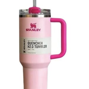 May include: A pink Stanley Quencher H2.0 Tumbler with a matching pink handle and straw. The tumbler has a white label with black text that reads "THE FLOWSTATE QUENCHER H2.0 TUMBLER". The Stanley logo is visible.