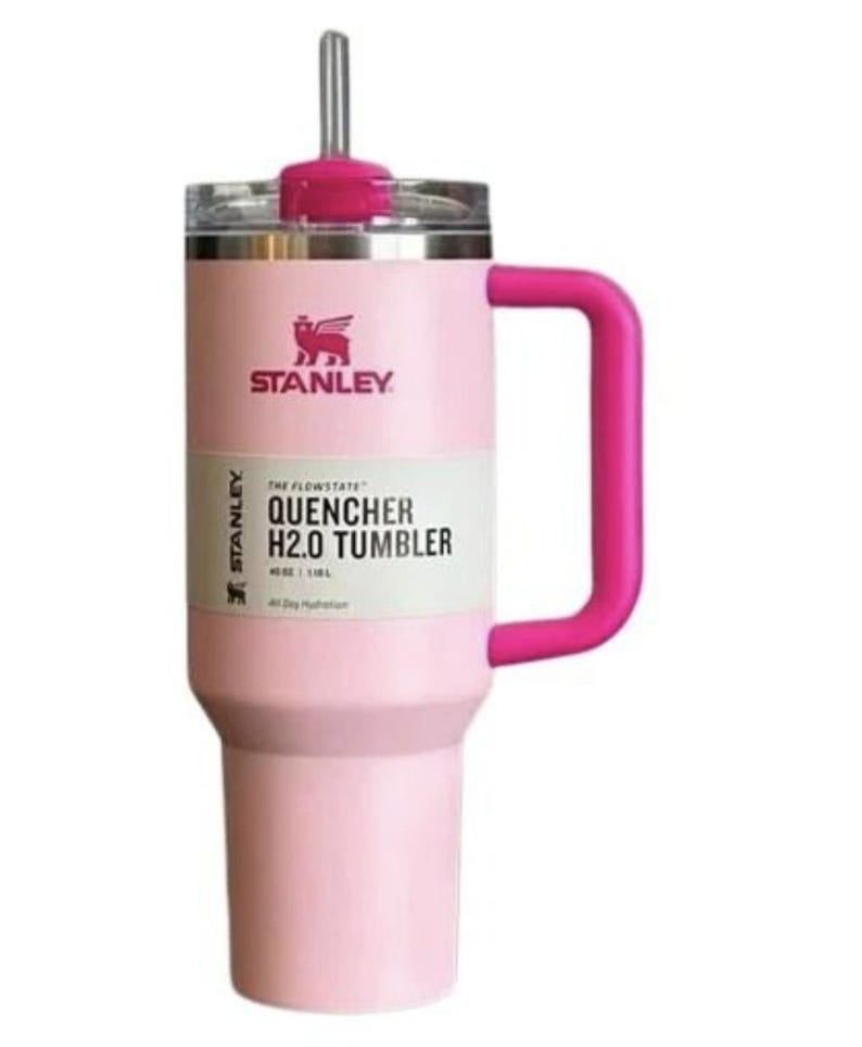 May include: A pink Stanley Quencher H2.0 Tumbler with a matching pink handle and straw. The tumbler has a white label with black text that reads "THE FLOWSTATE QUENCHER H2.0 TUMBLER". The Stanley logo is visible.