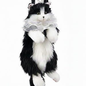 May include: A plush cat-shaped backpack in black and white, featuring a ruffled white collar and black leather straps. The cat has a fluffy appearance with white paws and a tail, designed to be worn on the back.