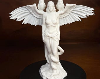 May include: A white sculpture of a woman with outstretched wings, two owls, and a snake wrapped around her. The statue is on a black base, with a dark brown background.