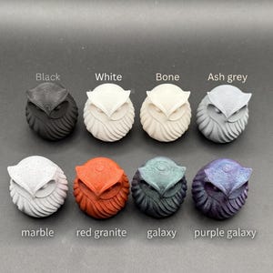 May include: Eight small owl figurines arranged in two rows. The top row includes black, white, bone, and ash grey owls. The bottom row features marble, red granite, galaxy, and purple galaxy owls. Each owl has a textured, rounded body design.