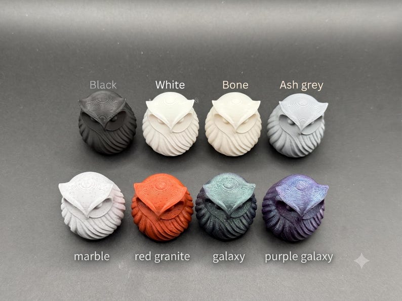 May include: Eight small owl figurines arranged in two rows. The top row includes black, white, bone, and ash grey owls. The bottom row features marble, red granite, galaxy, and purple galaxy owls. Each owl has a textured, rounded body design.