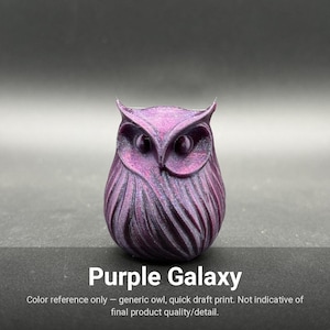 May include: A small, stylized owl figurine featuring a deep purple and black iridescent finish with a textured, layered feather pattern. The object displays prominent circular eyes and pointed ear tufts, with the text Purple Galaxy printed below.