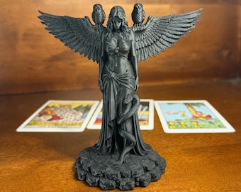 Puede incluir: Una figura de color negro mate con alas sobre una base rocosa. La figura tiene grandes alas emplumadas, un búho posado en cada hombro y una serpiente enroscada alrededor de la parte inferior del cuerpo. Viste un top y una prenda drapeada.