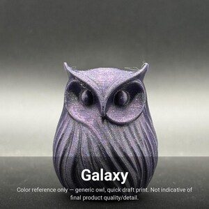 May include: A small, three-dimensional owl figurine with a dark purple, shimmering, glitter-like finish. The owl features prominent ear tufts, large circular eyes, and detailed, layered feather textures across its body. The word Galaxy is printed below.