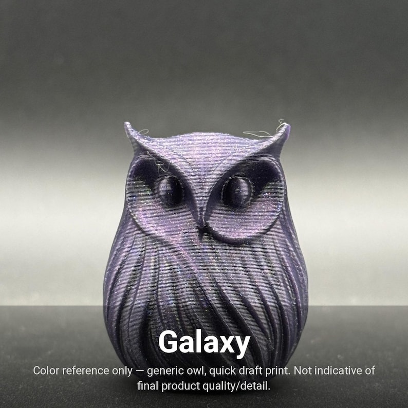May include: A small, three-dimensional owl figurine with a dark purple, shimmering, glitter-like finish. The owl features prominent ear tufts, large circular eyes, and detailed, layered feather textures across its body. The word Galaxy is printed below.
