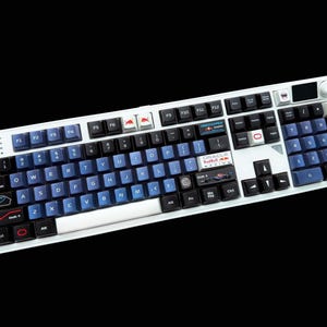May include: A white mechanical keyboard featuring a custom keycap set with blue and black keys. The layout includes specialised branding, including Oracle Red Bull Racing logos, Formula 1 imagery, and various racing-themed icons on specific keys.