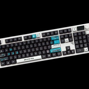 Puede incluir: Un teclado mecánico blanco y negro con teclas personalizadas en color verde azulado y blanco con la marca Mercedes-AMG Petronas Formula One Team, incluyendo el logotipo AMG en la barra espaciadora y varios gráficos de carreras en teclas.