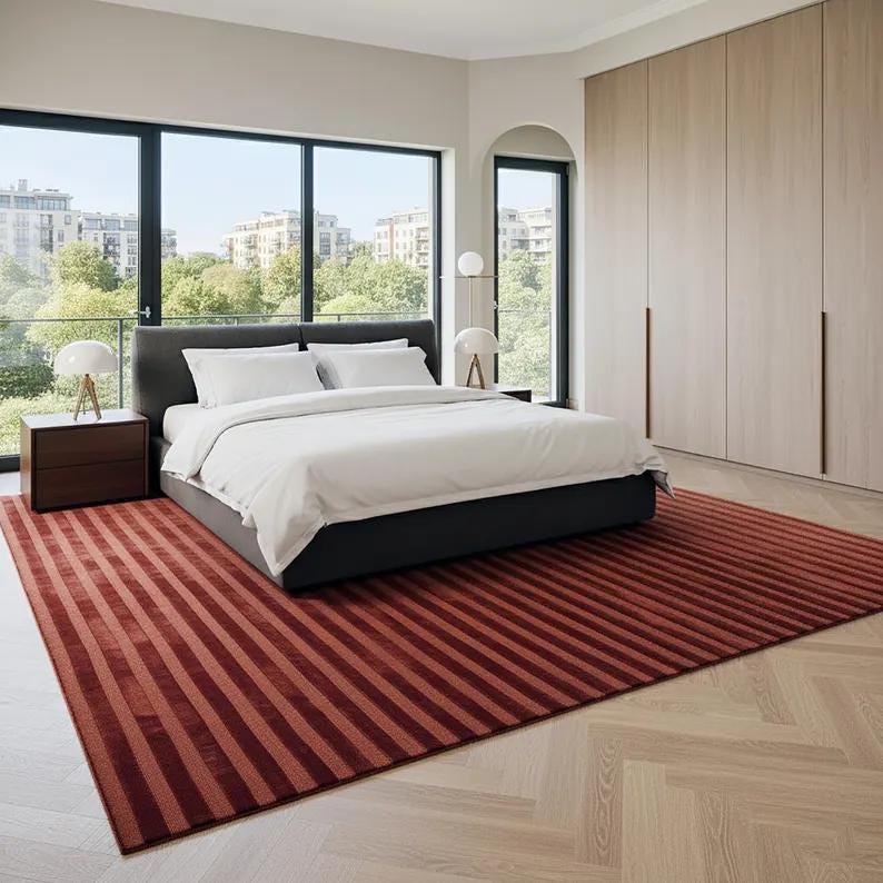 Pu&ograve; includere: Una camera da letto moderna con un letto con biancheria da letto bianca, testiera grigio scuro e tappeto a righe rosse. La stanza ha grandi finestre, mobili in legno e una palette di colori neutri.