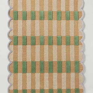 May include: A rectangular rug with a scalloped edge. The rug features a pattern of vertical stripes in tan and white, intersected by green rectangular blocks. The border is a light grey colour.