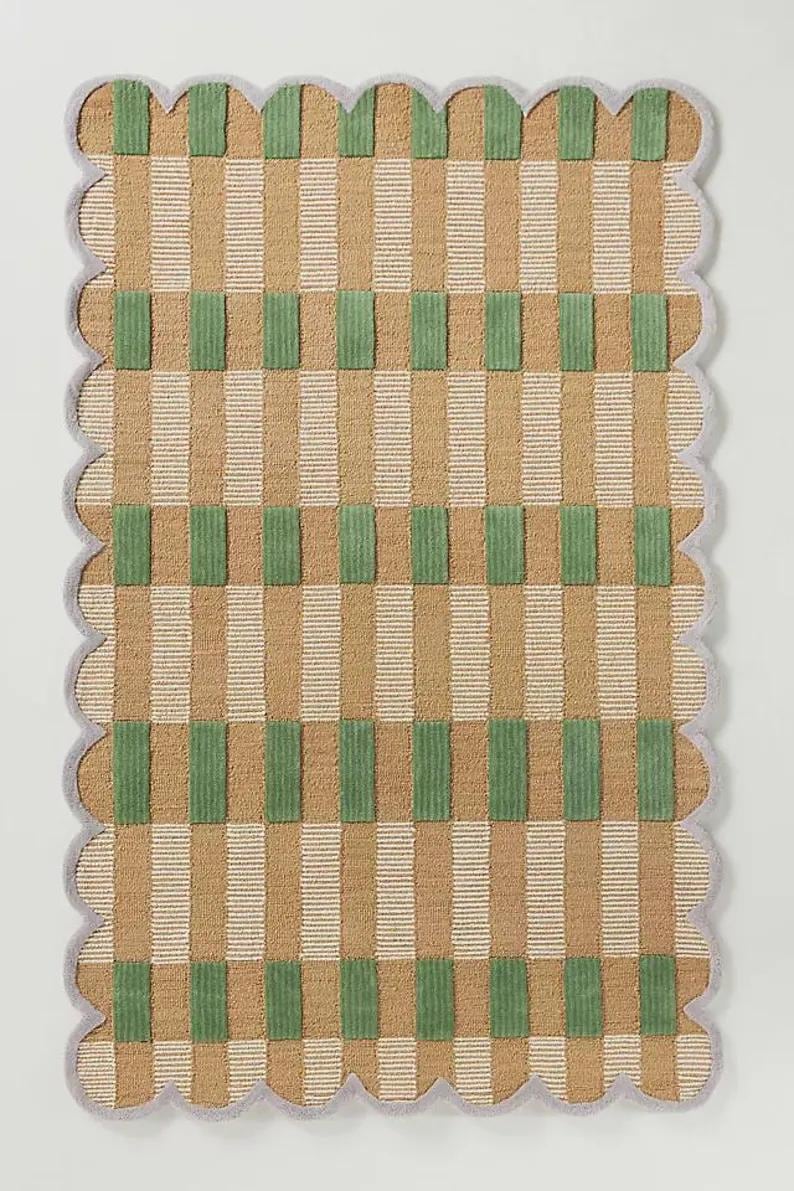 May include: A rectangular rug with a scalloped edge. The rug features a pattern of vertical stripes in tan and white, intersected by green rectangular blocks. The border is a light grey colour.