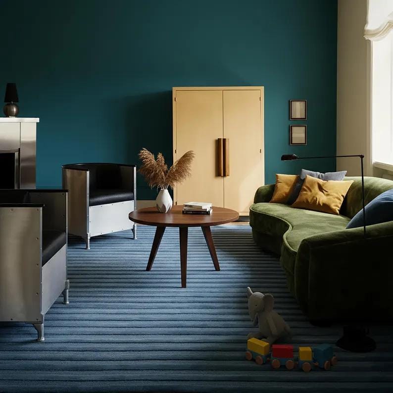 Pu&ograve; includere: Un moderno soggiorno con una parete verde acqua, un tappeto a righe blu e un divano in velluto verde. Un tavolino rotondo in legno con un vaso di piante secche. Due sedie nere e argentate e un armadio beige.