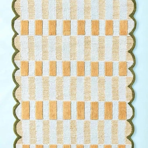 May include: A rectangular rug featuring a repeating pattern of vertical white and orange stripes, with orange rectangles. The rug has a scalloped green border.