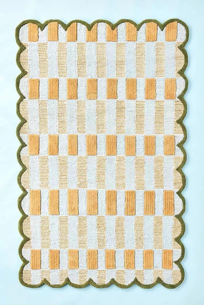 May include: A rectangular rug featuring a repeating pattern of vertical white and orange stripes, with orange rectangles. The rug has a scalloped green border.
