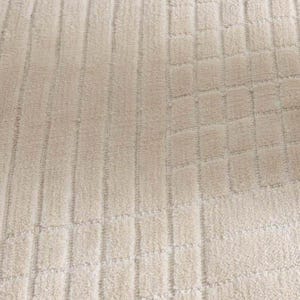 Pu&ograve; includere: Primo piano di un tessuto beige strutturato con un motivo ripetuto di linee verticali e blocchi quadrati. Il tessuto ha un aspetto morbido e felpato, che suggerisce un tappeto o un tessuto.