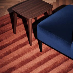 Pu&ograve; includere: Un tavolino in legno scuro con gambe affusolate &egrave; appoggiato su un tappeto a righe color ruggine. Una panca imbottita blu navy con gambe nere &egrave; a destra. La scena &egrave; ambientata su un pavimento in legno.