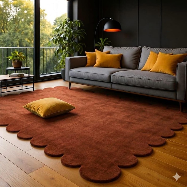 May include: A living room scene featuring a gray sofa with mustard-colored pillows, a rust-colored scalloped rug, and a mustard-colored floor cushion. A black floor lamp and a large window with a view of trees complete the decor.