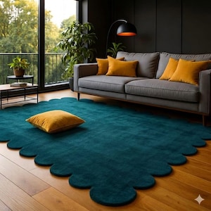May include: A teal scalloped-edge rug with a mustard yellow square pillow on a hardwood floor. A gray sofa with mustard yellow pillows sits against a dark wall. A black floor lamp and potted plants complete the living room setting.