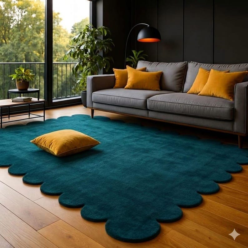 May include: A teal scalloped-edge rug with a mustard yellow square pillow on a hardwood floor. A gray sofa with mustard yellow pillows sits against a dark wall. A black floor lamp and potted plants complete the living room setting.