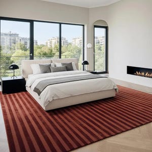 Pu&ograve; includere: Una camera da letto moderna con un letto grande, un tappeto rosso a righe e ampie finestre con vista su un paesaggio urbano. Il letto ha lenzuola bianche e cuscini grigi. Due lampade nere sono sui comodini. Un camino &egrave; sul muro.