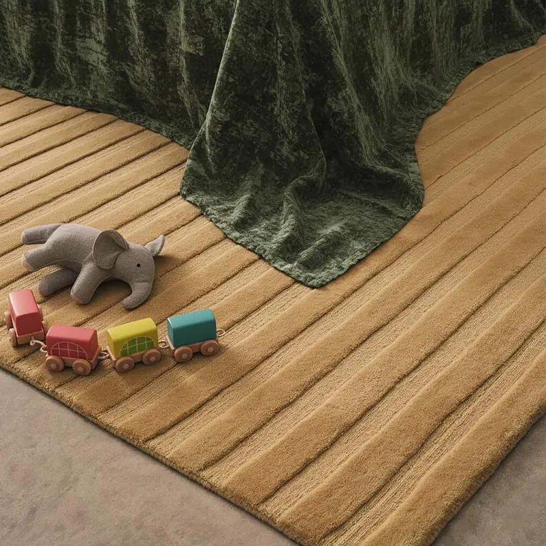Pu&ograve; includere: Un tappeto beige a coste con una coperta verde drappeggiata sopra. Un elefante di peluche grigio e un set di trenini in legno colorati sono sul tappeto. I vagoni sono rossi, rosa, gialli e blu.
