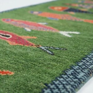 May include: A green rectangular rug with a repeating pattern of colorful fish. The fish are red, orange, and blue, with white fins and black details. The rug has a dark blue border.
