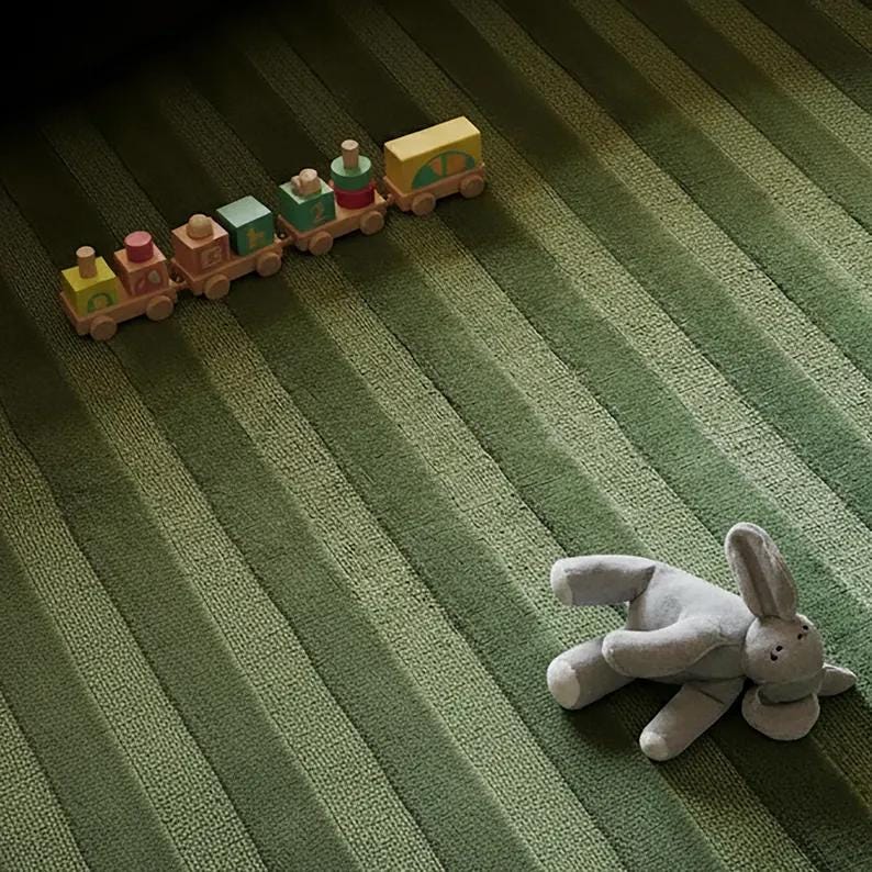 Pu&ograve; includere: Un trenino giocattolo in legno con blocchi colorati e un coniglietto di peluche grigio su un tappeto verde a righe. Il treno ha una locomotiva gialla, vagoni rosa, verdi e marroni. Il coniglietto &egrave; sdraiato su un fianco.