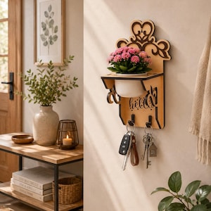 May include: Wooden key holder with a decorative floral design, a small white planter with pink flowers, and the word "hello". Includes key hooks with keys hanging from them.