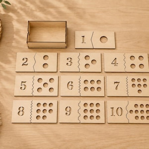 Könnte beinhalten: Holz-Zahlenpuzzleset mit den Zahlen 1-10, jeweils in zwei Teile geteilt. Die Zahlen sind in das Holz geätzt, und die entsprechende Anzahl an Punkten oder ein Kreis befinden sich auf der anderen Hälfte. Enthält eine kleine Holzkiste zur Aufbewahrung.