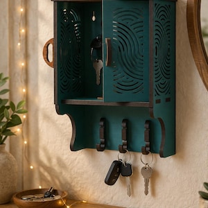 Könnte beinhalten: Ein teal-farbener und brauner Schlüsselhalter aus Holz mit einer Schranktür und Schlüsselhaken. Die Schranktür hat ein dekoratives Ausschnittdesign. Schlüssel hängen an den Haken und im Schrank.
