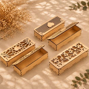 Puede incluir: Cajas rectangulares de madera clara con diseños decorativos cortados con láser. Algunas cajas tienen tapas abiertas. Una vela en un portavelas de cristal está en el fondo. Las cajas están sobre una superficie neutra.