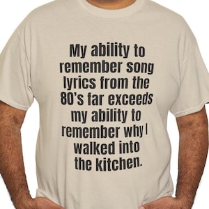 May include: A man wearing a light beige t-shirt with the text "My ability to remember song lyrics from the 80's far exceeds my ability to remember why I walked into the kitchen."