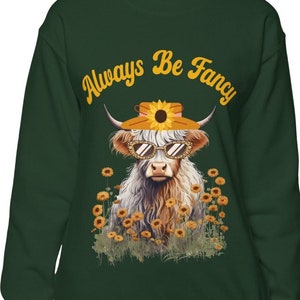 May include: A dark green sweatshirt with a white cow wearing sunglasses and a sunflower hat. The text "Always Be Fancy" is printed in yellow on the sweatshirt.