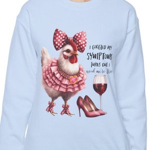 May include: A light blue sweatshirt with a graphic of a chicken wearing a pink dress, a red bow, and high heels. The chicken is holding a glass of red wine. The text on the sweatshirt reads "I googled my symptoms turns out I need more wine."
