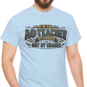 May include: Light blue t-shirt with the text "I'M AN AG TEACHER BY CHOICE NOT BY CHANCE" in a decorative design. The shirt is a short-sleeved crew neck style.