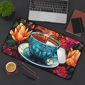May include: A rectangular desk mat featuring a stained-glass design with a blue teacup and saucer filled with tea. The mat has a floral pattern with orange and red flowers, a white mouse, and a laptop.