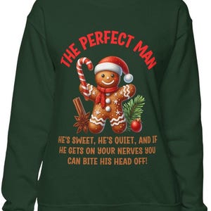 May include: Dark green sweatshirt with the text "THE PERFECT MAN" in red. A gingerbread man wearing a Santa hat and scarf is featured, holding a candy cane. The text below reads "HE'S SWEET, HE'S QUIET, AND IF HE GETS ON YOUR NERVES YOU CAN BITE HIS HEAD OFF!"