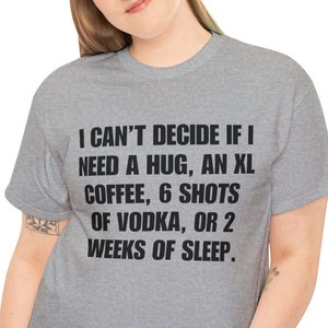 May include: A heather grey t-shirt with a humorous saying: "I can't decide if I need a hug, an XL coffee, 6 shots of vodka, or 2 weeks of sleep."