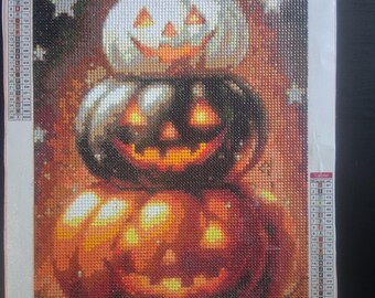 Puede incluir: Kit de pintura de diamantes con tres calabazas apiladas con caras sonrientes. Las calabazas son de color naranja, negro y blanco, con un fondo estrellado. El tamaño del kit es de 30 x 40 cm.