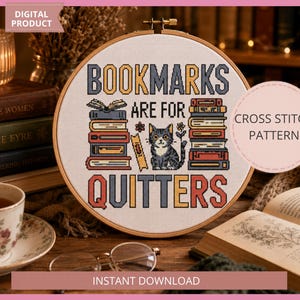 May include: A circular wooden embroidery hoop containing a cross stitch pattern on white fabric. The design features stacks of colorful books, a small cat, and the text "BOOKMARKS ARE FOR QUITTERS" in bold, multi-colored block lettering.