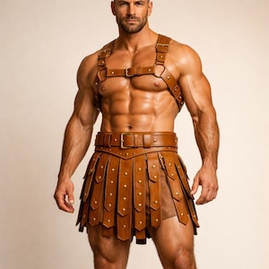 Op de afbeelding: Bruin leren harnas en rok set met goudkleurige klinknagels en gespen. Het harnas heeft schouderbanden en borstriemen, terwijl de rok verticale panelen heeft. De set is ontworpen met een gladiatorthema.